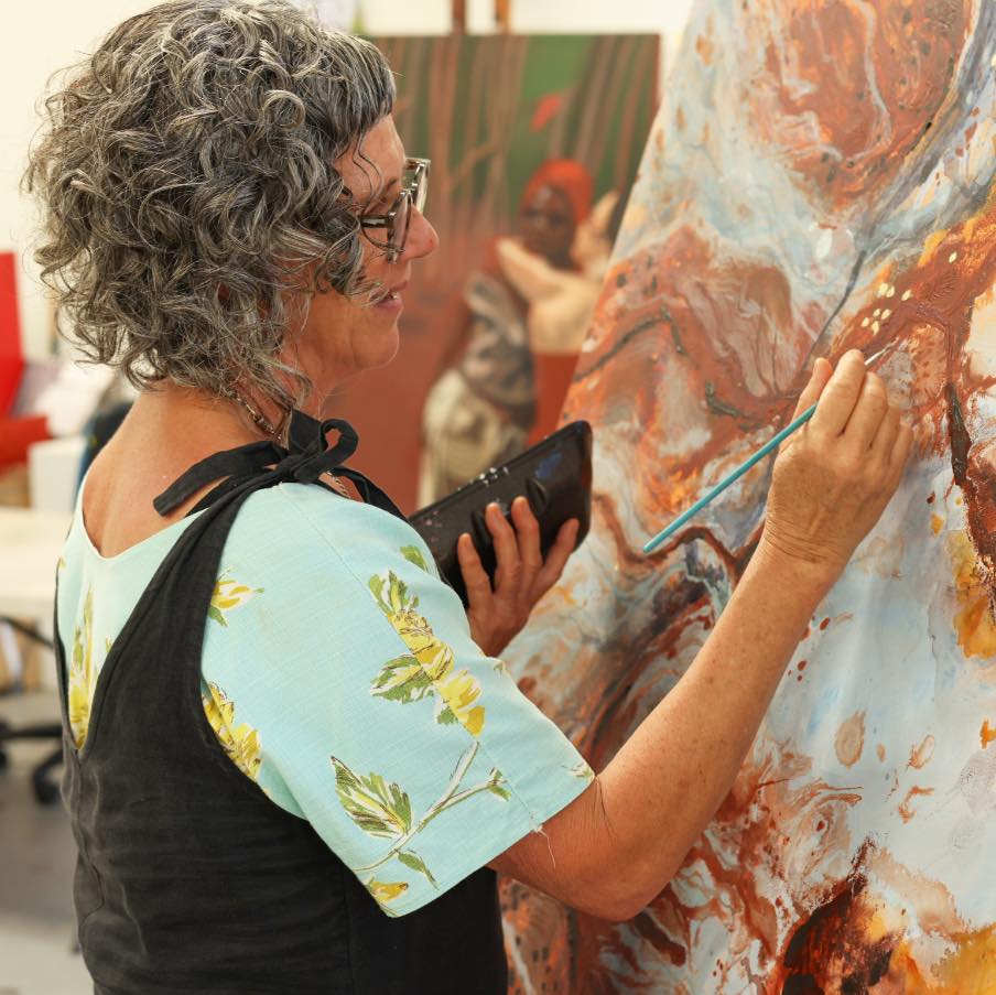 Woman painting a large artwork with a tablet in an art studio.
